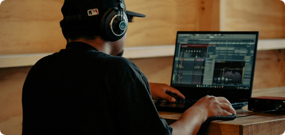 Productor musical con audífonos profesionales editando pistas de audio en un notebook de alto rendimiento, conectado a una interfaz de sonido externa en un estudio casero.