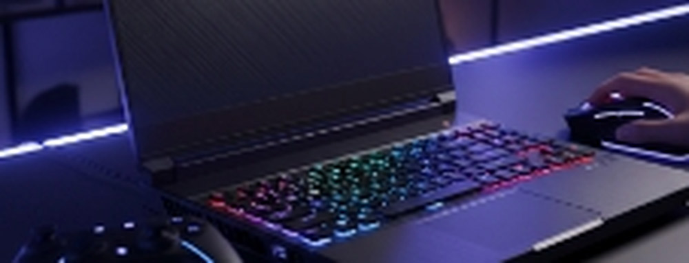 Notebook gamer con teclado retroiluminado RGB en un setup oscuro con iluminación LED azul. En primer plano se ve un control de videojuegos y una mano utilizando un mouse gamer.